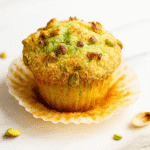 Freshly baked pistachio muffin with golden top and chopped pistachios on white marble