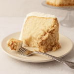 A slice of Tom Cruise coconut cake on a plate with a forkful ready to eat, showing moist cake and coconut frosting