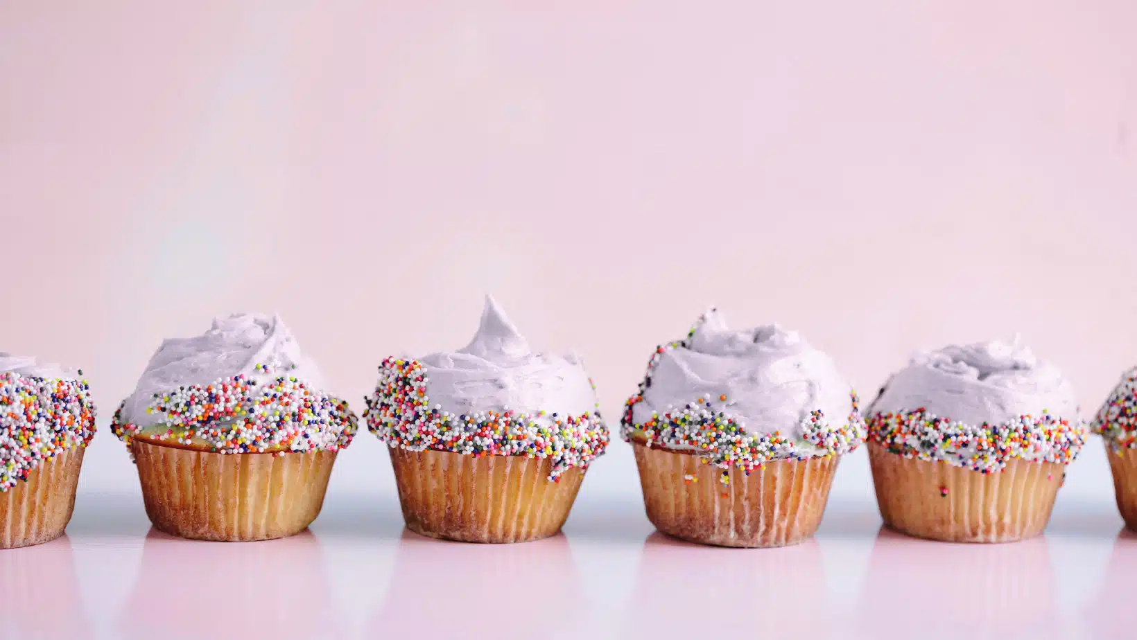 Home 1 Colorful frosted cupcakes with sprinkles on a pink background