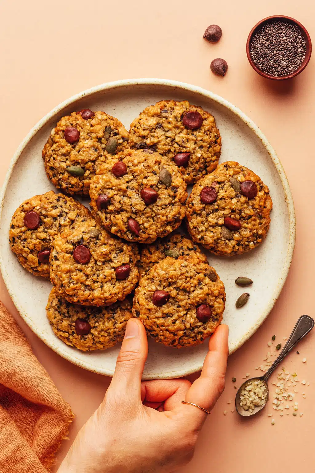 Freshly baked seedy quinoa breakfast cookies stacked on a rustic ceramic plate with a hand holding one cookie