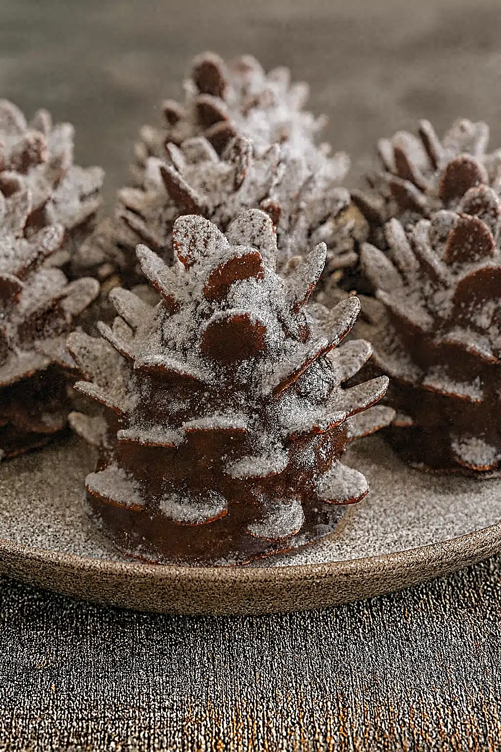 Chocolate-covered pine cone brownies dusted with powdered sugar, served on a beige plate.