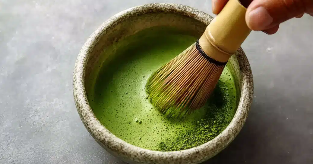 banana-bread-matcha-whisking whisking banana bread matcha in a ceramic bowl with bamboo whisk