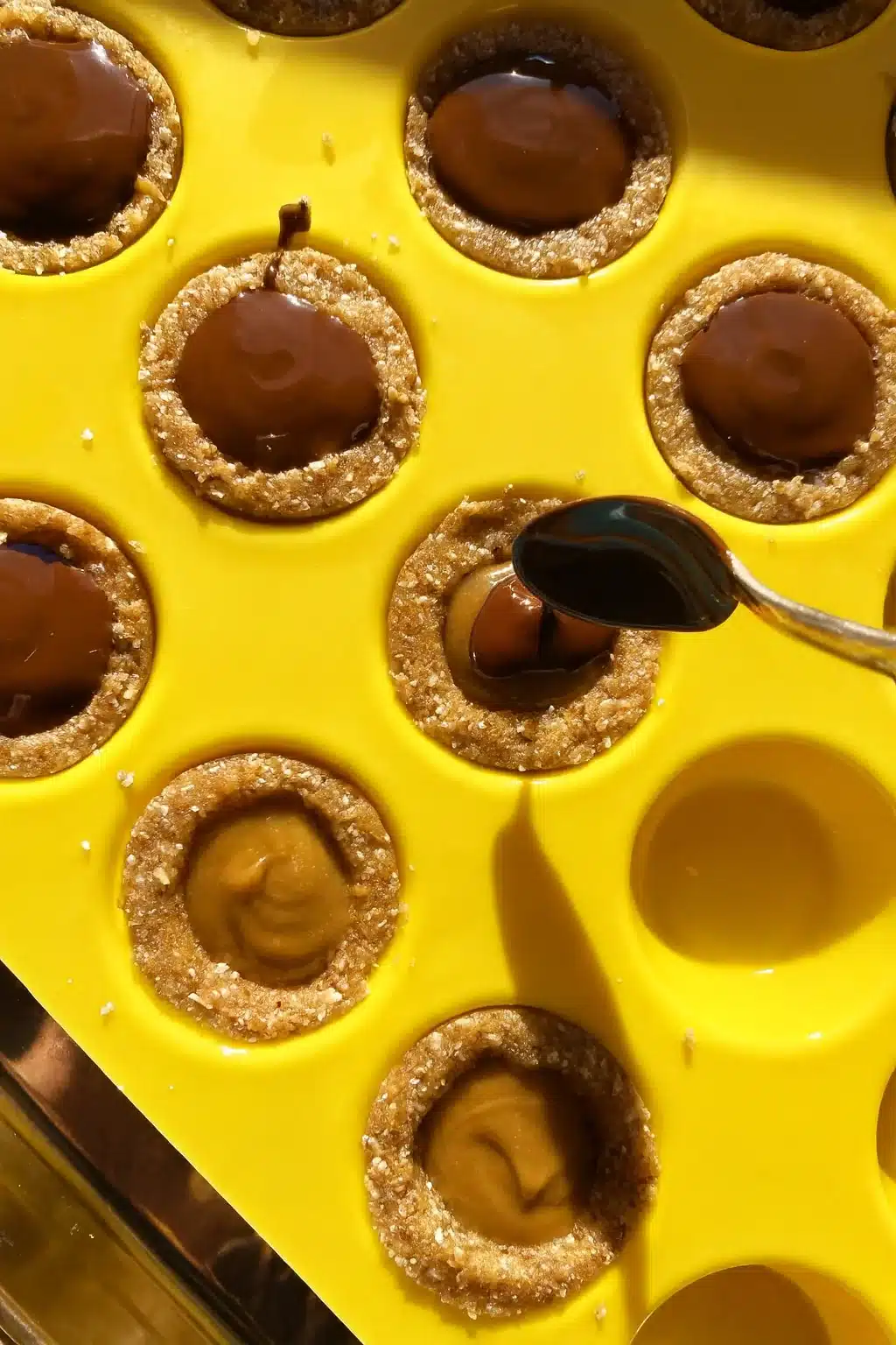 Pouring chocolate onto healthy Twix cookie cups with a spoon