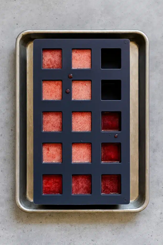 Pouring homemade strawberry gummies mixture into silicone molds